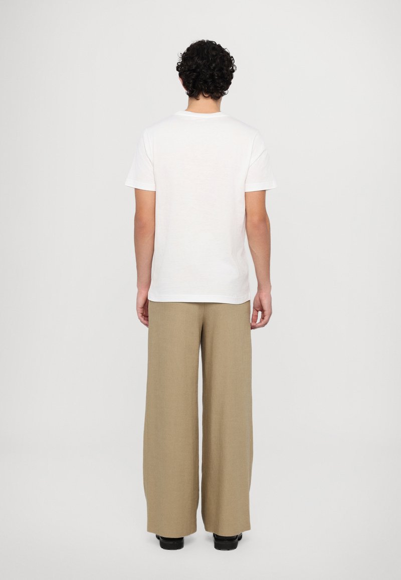White, short-sleeve t-shirt paired with loose, beige trousers. The fabric appears smooth, with no visible patterns or accents.
