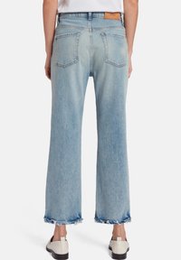 Jeans a gamba larga celesti con orli sfrangiati, dotati di vita media e due tasche posteriori. Il tessuto sembra morbido e leggermente usurato.
