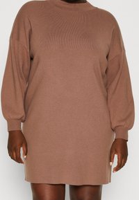 Strickkleid mit langen Ärmeln in einem gedämpften Braunton. Es hat einen hohen Halsauschnitt und eine lockere Passform mit leicht gepufften Ärmeln, gefertigt aus weichem Stoff.