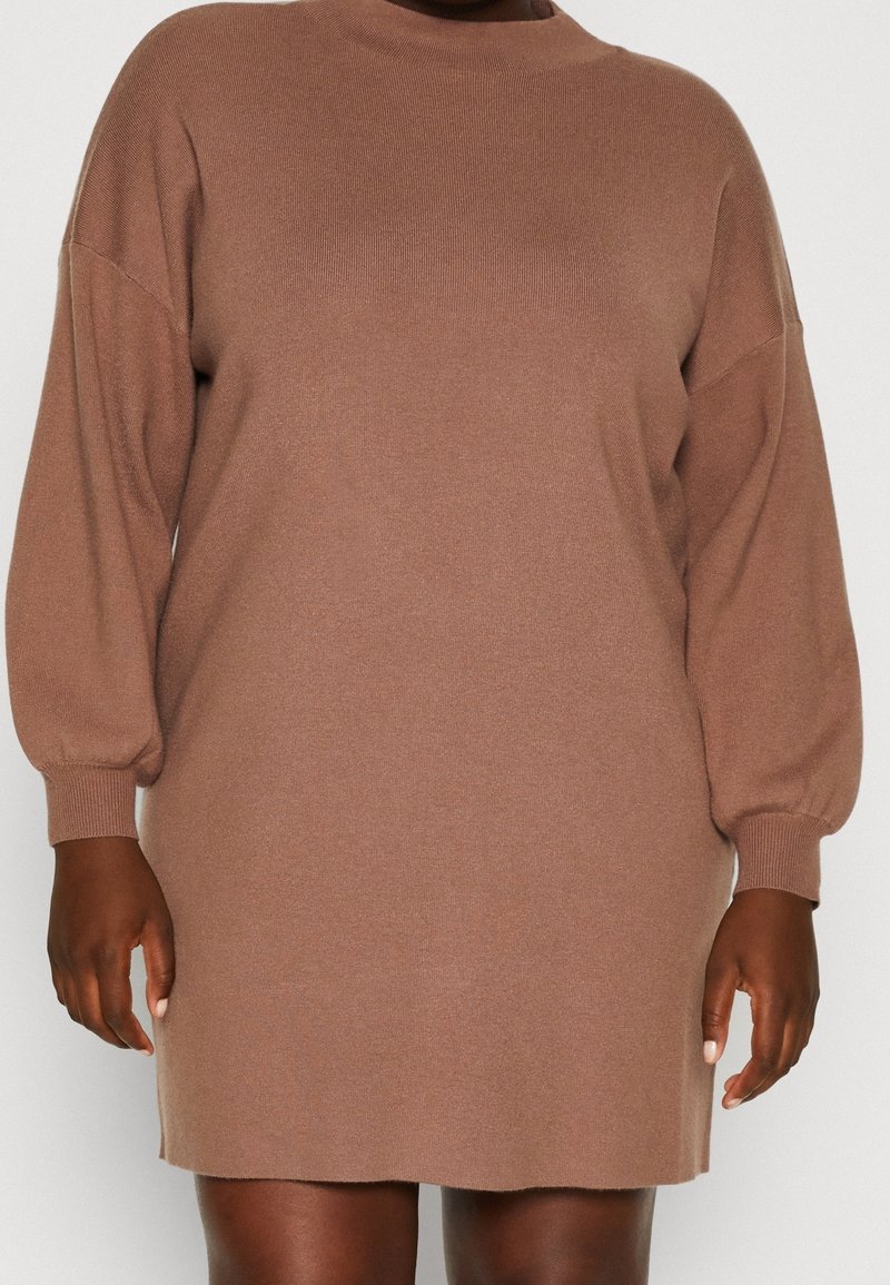 Strickkleid mit langen Ärmeln in einem gedämpften Braunton. Es hat einen hohen Halsauschnitt und eine lockere Passform mit leicht gepufften Ärmeln, gefertigt aus weichem Stoff.