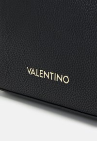 Black textured leather bag featuring a gold embossed "VALENTINO" logo on the front, with a smooth surrounding surface.