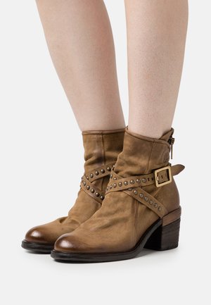 Brown leather ankle boots with a slouchy design, studded strap, and a gold buckle, featuring a low stacked heel.