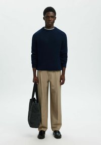 Jūras spēku zilas ribotas adījuma džemperis, bēšas pielāgotas bikses, melnas ādas kurpes un tumši pelēks auduma pleca soma. Minimālistisks dizains, neitrālas krāsas.