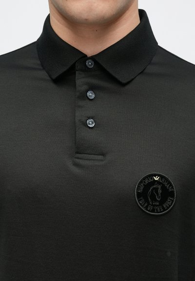 Juoda polo marškinėliai su tekstūruotu apykakle, trijų sagų stulpeliu ir siuvinėta apvali dėmė krūtinėje su arkliu ir prekės ženklo pavadinimu.