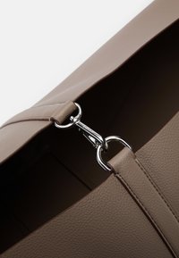 Geantă din piele bej cu o suprafață texturată, având un închizător din metal argintiu și accente cusute pe margini.