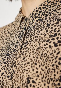 Gros plan sur une chemise beige à motif léopard noir avec un col pointu sur la partie supérieure de la poitrine et du cou d'une personne.