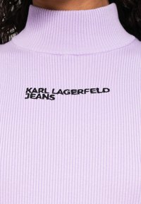 Lavandos spalvos riboto audinio golfas su siuvinėtu juodu "KARL LAGERFELD JEANS" logotipu, įsiuvu po apykakle.