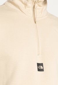 Felpa con zip a un quarto beige, con colletto alto e un piccolo logo quadrato nero di The North Face sul petto.