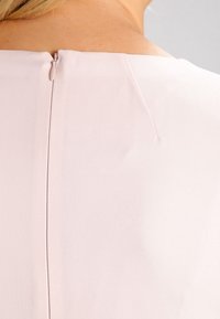 Ljusrosa klänning med en slät textur, med en dold dragkedja bak och en enkel, elegant halsringning.