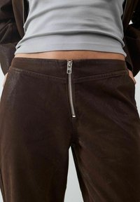 Bruine leren broek met een gestructureerde afwerking en een zichtbare zilveren rits aan de voorkant. Heeft een hoge taille.