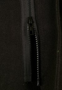 Veste en polaire noire avec un gros plan sur une fermeture éclair robuste noire, présentant un tissu texturé et des coutures contrastantes le long de la couture.