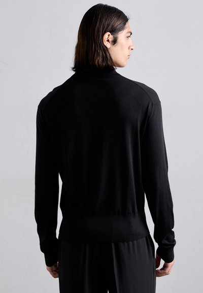 Suéter negro de manga larga con un diseño ajustado, confeccionado con material suave. Presenta un dobladillo y puños acanalados, textura lisa y un cuello redondo.
