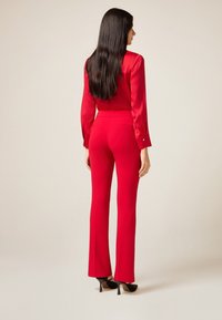 Rode satijnen blouse en nauwsluitende rode broek met uitlopende pijpen, met een gladde textuur en minimalistisch ontwerp. Achteraanzicht, zonder patronen.