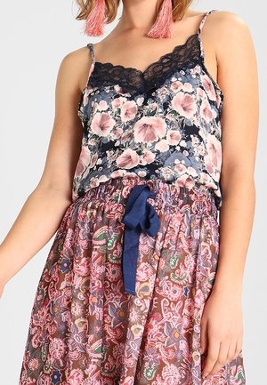 Woman wearing floral camisole with black lace trim and a high-waisted skirt with pink and purple floral patterns tied with a navy blue bow.