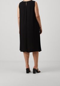 Svart ärmlös klänning med en avslappnad passform och nyckelhål baktill. Slätt tyg, knälång, kompletterad med svarta blockklacksandaler.