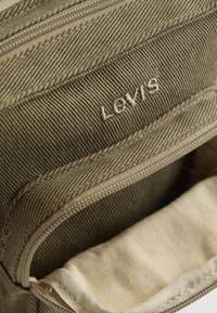 Close-up of an open khaki canvas bag with visible zipper and Levi’s logo embroidered on the fabric.