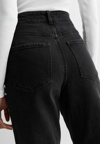 Jeans neri a vita alta con una trama denim liscia, dotati di due tasche posteriori e un design aderente in prossimità della vita e dei fianchi.