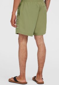 Shorts de bain verts avec une taille élastique, des poches latérales et un logo imprimé verticalement en blanc sur le côté gauche.