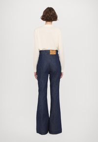 Högmidjade utställda jeans i mörkblå denim. Har fickor med hjärtformad bak och kontrasterande sömmar. Bärs med en krämfärgad långärmad topp.