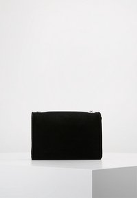 Black rectangular suede handbag with silver chain strap, displayed on a white pedestal against a plain light background.