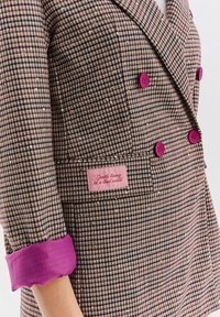 Hnedo-krémové sako s psím zubom a flitrami. Má ružové gombíky a fialové manžety. Štítok nesie nápis "Gentle living in a loud world."