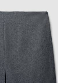 Tissu gris avec une texture subtile, présentant un ourlet droit et un détail fendu près du bas. Le matériau semble léger et raffiné.