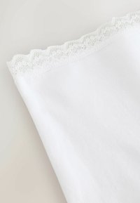 Balts kokvilnas apģērbs ar mežģīņu maliņu augšējā malā, raksturots ar gludu, mīkstu tekstūru un tīru apdari.