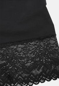 Svart klänning med en mjuk ovandel och spetskant. Spetsen har blommönster och scalloped kanter, vilket ger en kontrast i textur.