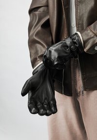 Sorte læderhandsker med en glat tekstur, tætsiddende design og knapdetalje, med buede fingre og en tætsiddende håndledsområde.