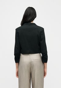 Μαύρο κοντό σακάκι με μακριά μανίκια, διπλωμένα μανσέτα και κλασικό γιακά, συνδυασμένο με μπεζ ριγωτό ψηλόμεσο παντελόνι.