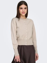 Cardigan beige tricoté avec un col rond, des manches longues et un ourlet court, doté d'une rangée de boutons argentés sur le devant.