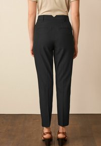 Pantalons noirs ajustés avec une taille mi-haute et une coupe droite. Comprend deux poches arrière et une texture lisse.
