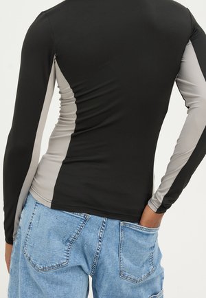 Haut à manches longues avec panneaux noirs et gris, fabriqué en tissu extensible lisse, avec une coupe ajustée et un ourlet arrondi à l'arrière.