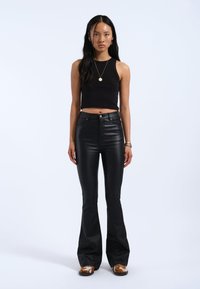 Zwarte cropped tanktop gecombineerd met zwarte hoge taille flared pants. Het materiaal lijkt soepel met minimale hardware. Bruine en witte schoenen.