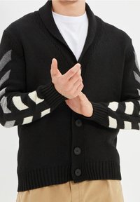 Cardigan nero lavorato a maglia con colletto scialle e cinque bottoni neri. Presenta strisce diagonali bianche e grigie sulle maniche.