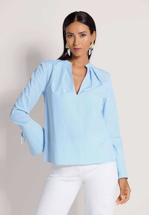 Hellblaue Bluse mit Streifen, V-Ausschnitt und plissiertem Detail. Lange Ärmel mit Glockenform und Bändern an den Manschetten. Glatte Textur.