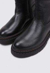 Bottines en cuir noir avec une finition texturée, bout rond et couture contrastante marron foncé sur une semelle en caoutchouc épaisse.