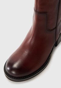 Bota de cuero marrón hasta el tobillo con punta redonda, textura suave, costuras sutiles y un bajo tacón negro. Diseño elegante sin adornos.