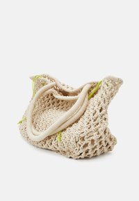 Sac en crochet beige avec un design texturé à maille ouverte. Il présente des poignées douces et arrondies ainsi que des liens d'accent verts vifs pour la fermeture.