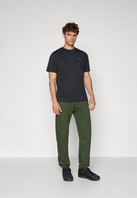 Tricou negru cu mânecă scurtă și guler rotund, asociat cu pantaloni de trening verzi. Țesătură texturată și siluetă ajustată. Adidași negri.