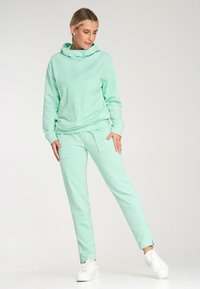 Jasno miętowy dres składający się z luźnej bluzy z kapturem i zwężanych spodni z przednimi kieszeniami, wykonany z miękkiego, gładkiego materiału.
