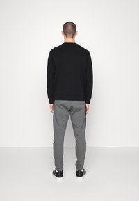 Svart långärmad sweatshirt med ribbade mudd, tillsammans med grå mjukisbyxor med sidostrimma, och svarta sneakers med vita sulor.