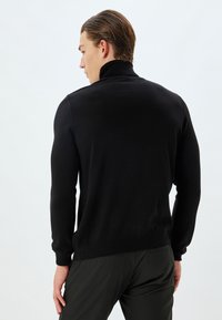Zwarte gebreide trui met een hoge kraag, geribbelde manchetten en een slim fit, gemaakt van een zachte stof, met een schone, gestructureerde afwerking.