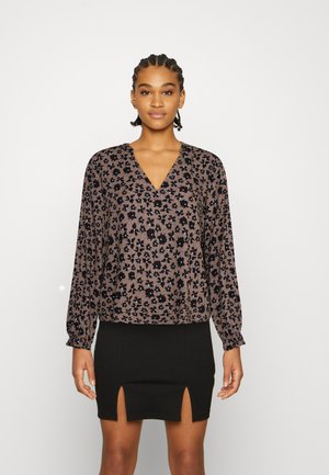 Blusa floral castanha com decote em V e mangas longas bufantes. Combinada com uma saia mini preta com duas aberturas frontais. Textura de tecido suave.