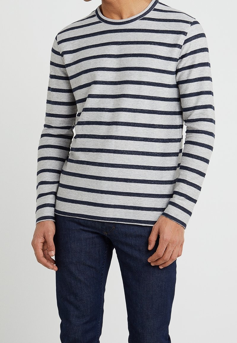 Chemise à manches longues gris clair avec des rayures horizontales bleu marine, col rond, en coton doux, associée à un jean en denim foncé.