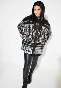 Svartvitt mönstrad oversized kofta med V-hals, knäppning fram och långa ärmar, matchad med svarta leggings och kängor.