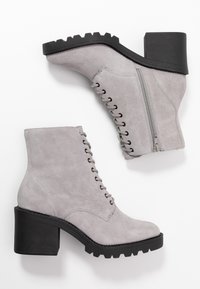 Botines de ante gris con un tacón negro grueso, que cuentan con cordones en la parte delantera, cremallera lateral y suela texturizada para mayor agarre.