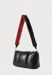 Μαύρη επενδυμένη δερμάτινη τσάντα ώμου με μαξιλαρωτό λουράκι που διαθέτει κόκκινο και μαύρο κείμενο. Χρυσά αξεσουάρ ολοκληρώνουν το σχέδιο.