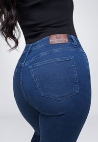 Blauwe denim jeans met een gladde textuur, voorzien van een bruine leren taillebandlabel en twee achterzakken. Ontworpen voor een aansluitende pasvorm.