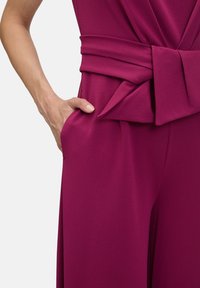 Fuchsia jumpsuit med bred, plisserad midja med knytband och sidofickor. Tillverkad av mjukt och slätt tyg med en flödande design.